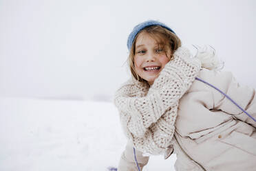 Playful girl smiling in warm clothing during winter - KMKF01508