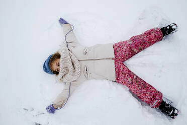 Playful girl making snow angel during winter - KMKF01513