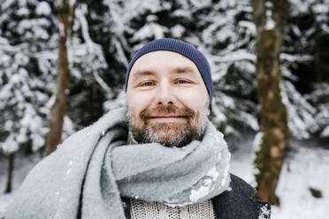 Lächelnder reifer Mann mit Schal im Schnee während der Ferien - KMKF01525