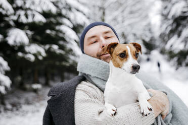 Man looking at Jack Russell Terrier dog during winter - KMKF01528