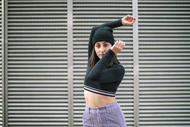 Young woman with arms raised standing against metallic shutter - GRCF00683