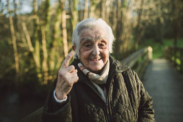 Elderly woman gesturing while standing on footbridge during winter - RAEF02430