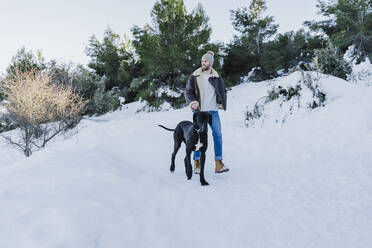 Young man and dog hiking on snow during winter - EBBF02377