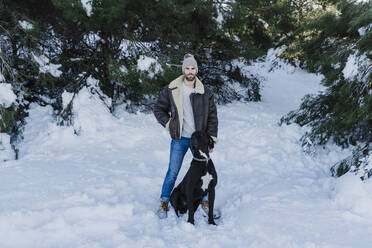 Mann mit Hund in verschneitem Land vor Bäumen stehend - EBBF02378