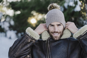 Smiling handsome man adjusting collar of jacket during winter - EBBF02379