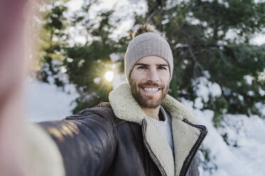 Happy young man taking selfie against trees in cold weather - EBBF02384