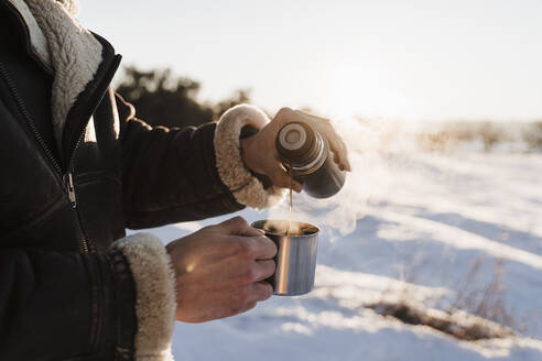 Mann gießt heißen Kaffee in Tasse durch Thermoskanne an einem sonnigen Tag - EBBF02387