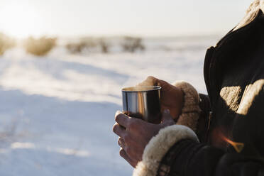 Young man holding coffee cup in cold weather on sunny day - EBBF02388