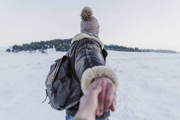Männlicher Rucksacktourist hält die Hand einer Frau während eines Spaziergangs im Schnee bei Sonnenuntergang - EBBF02395