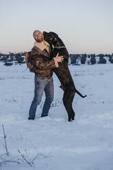 Playful Great Dane dog leaning on man in snow against clear sky - EBBF02396