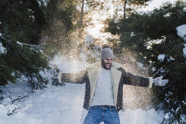 Fröhlicher Mann mit ausgestreckten Armen, der im Winter im Schnee spielt - EBBF02407