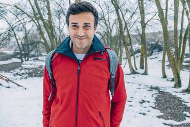 Lächelnder reifer männlicher Forscher in roter Jacke im Wald im Winter - IFRF00359