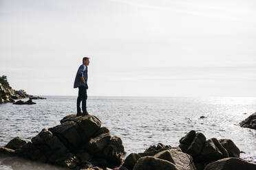 Mature man standing on rock while looking away against sea - JRFF05008