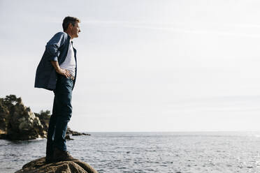 Man looking away while standing on rock against clear sky - JRFF05009