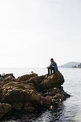 Man sitting on rock while looking away against sea - JRFF05013