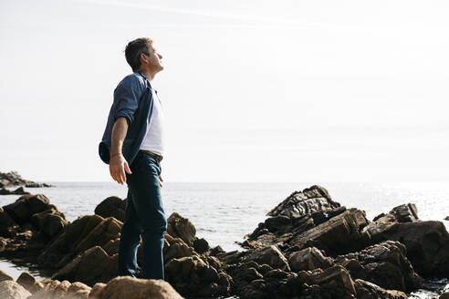 Genießen Sie reifen Mann stehend inmitten von Felsen am Meer während sonnigen Tag - JRFF05015