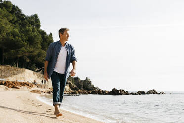 Älterer Mann, der an einem sonnigen Tag am Strand gegen den klaren Himmel läuft - JRFF05016