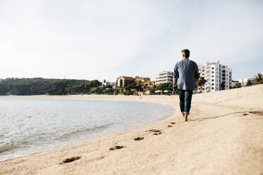 Man walking on beach during sunny day - JRFF05017