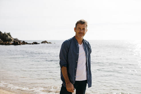 Lächelnder reifer Mann steht am Strand gegen das Meer - JRFF05021