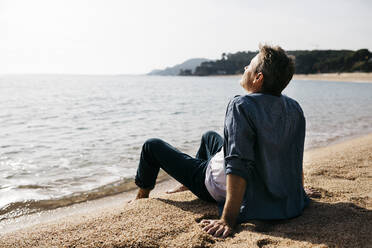 Relaxed man sitting on shore at beach during sunny day - JRFF05026