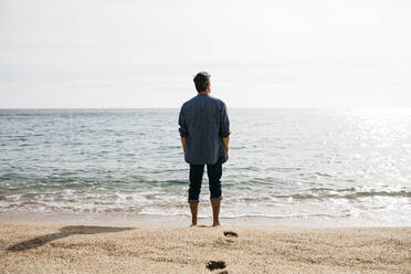 Mann steht an einem sonnigen Tag am Strand am Meer - JRFF05027