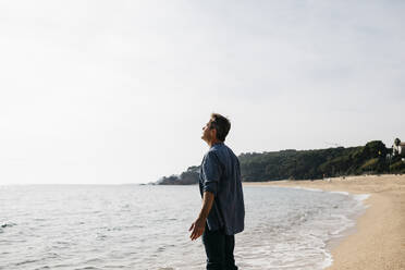 Man with arms outstretched enjoying at beach during sunny day - JRFF05030