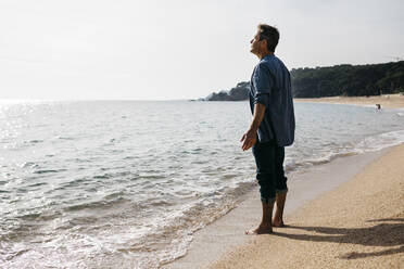 Mature man standing by water's edge at beach - JRFF05031