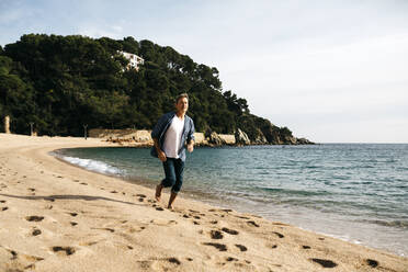 Mann läuft am Strand gegen einen Hügel an einem sonnigen Tag - JRFF05032