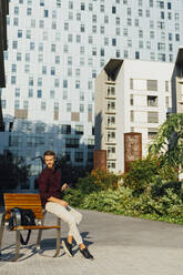 Male entrepreneur with mobile phone looking away while sitting in city - BOYF01661