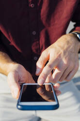 Businessman pointing at mobile phone screen while sitting outdoors - BOYF01673