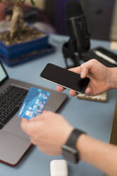 Businessman with credit card doing shopping over mobile phone at home - BOYF01713