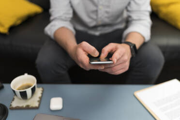 Businessman using mobile phone while sitting on sofa at home - BOYF01721