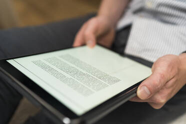 Geschäftsmann liest ein Dokument über ein digitales Tablet bei der Arbeit zu Hause - BOYF01735