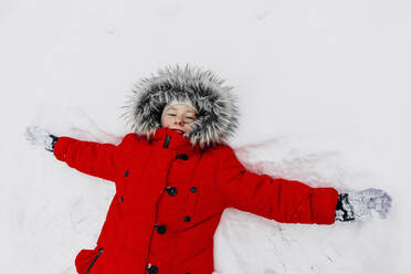 Girl in red warm clothing making snow angle during winter - OGF00828