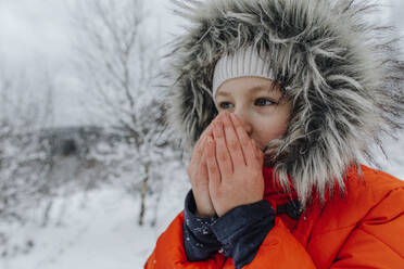 Small girl blowing on hands while looking away during winter - OGF00829