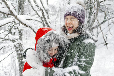 Fröhliches Mädchen im Teenageralter umarmt ihre Schwester, während es in den Ferien schneit - OGF00835