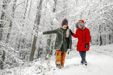 Teenage girl with sister walking on snow in forest during winter - OGF00836