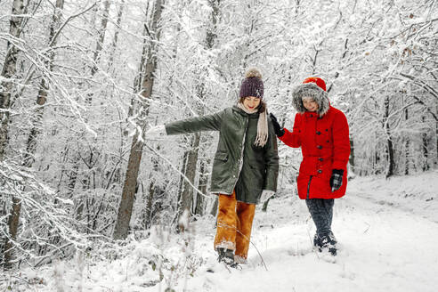 Teenager-Mädchen mit Schwester spazieren auf Schnee im Wald im Winter - OGF00836