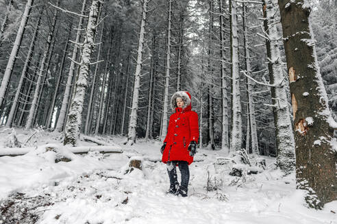 Small girl in red jacket standing on snow covered land at forest - OGF00838