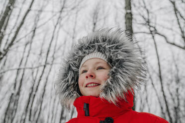 Smiling girl child wearing fur hat looking away in forest during vacations - OGF00839