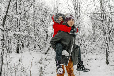 Teenager-Mädchen gibt Huckepack zu Schwester gegen Schnee bedeckt kahlen Bäumen im Wald - OGF00841