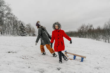 Teenager-Mädchen, das einen Schlitten zieht, während ein kleines Mädchen im Winter im Schnee läuft - OGF00843