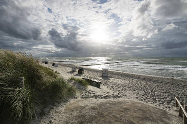 Sun setting over hooded beach chairs standing on empty beach - MYF02335