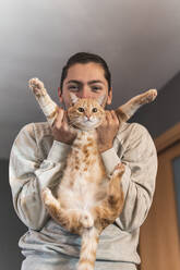 Young man playing with cat at home - JAQF00199