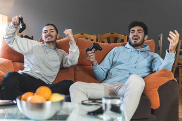 Junge wetteifernde Freunde spielen ein Videospiel auf dem Sofa im Wohnzimmer - JAQF00202