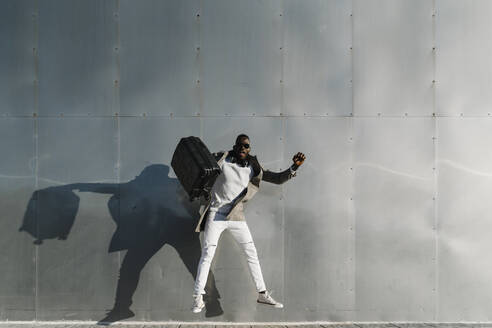 Man with suitcase jumping by metallic wall - MPPF01433