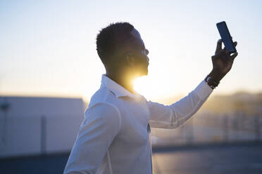 Mann nimmt Selfie auf Smartphone gegen Himmel während Sonnenuntergang - MPPF01452