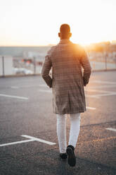 Man with hands in pockets walking at parking lot during sunset - MPPF01458