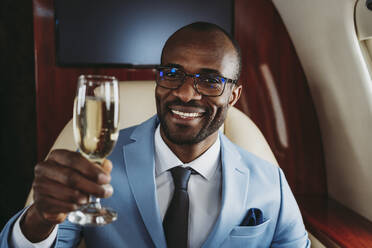 Lächelnder Geschäftsmann mit Champagner im Flugzeug - OIPF00254