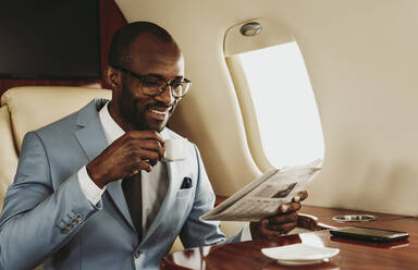 Lächelnder Geschäftsmann liest Zeitung und trinkt Kaffee im Flugzeug - OIPF00264